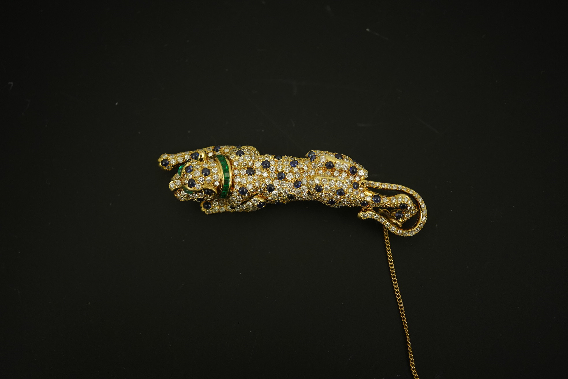 A modern Cartier style 18k gold, sapphire, emerald and diamond cluster set stalking panther brooch